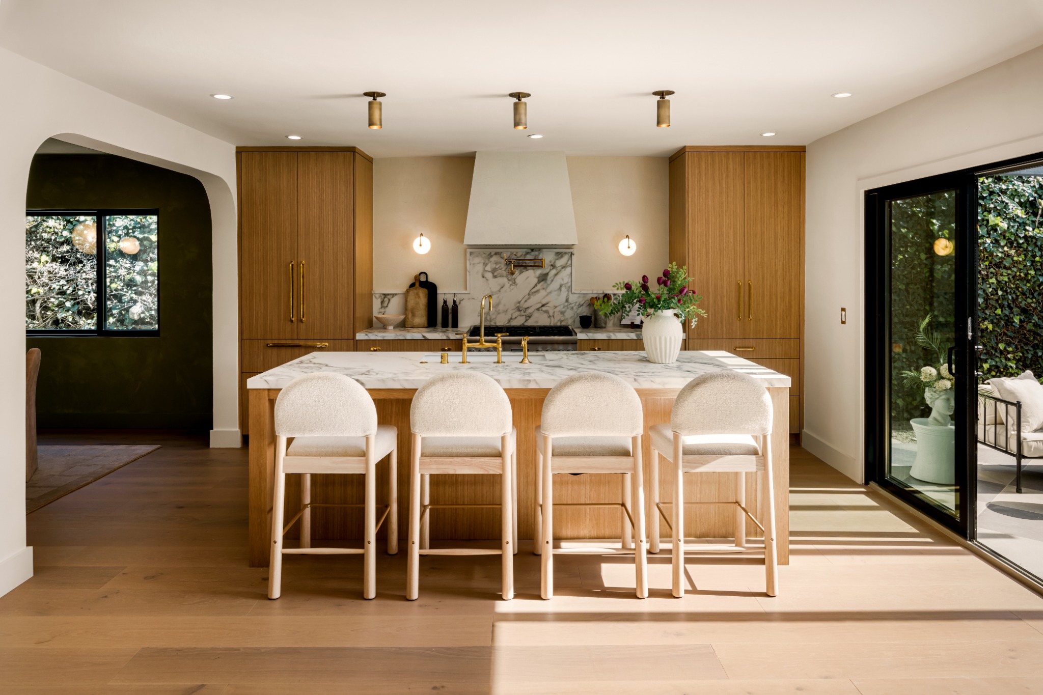 Bright kitchen with wood cabinetry, a marble island, and doors opening to a garden